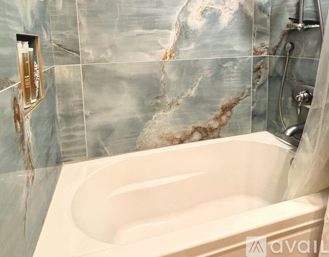 A bathroom with a marble patterned wall and a white bathtub.