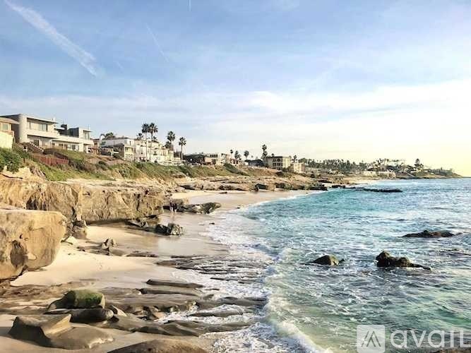A beach with clear water and a few buildings in the background.