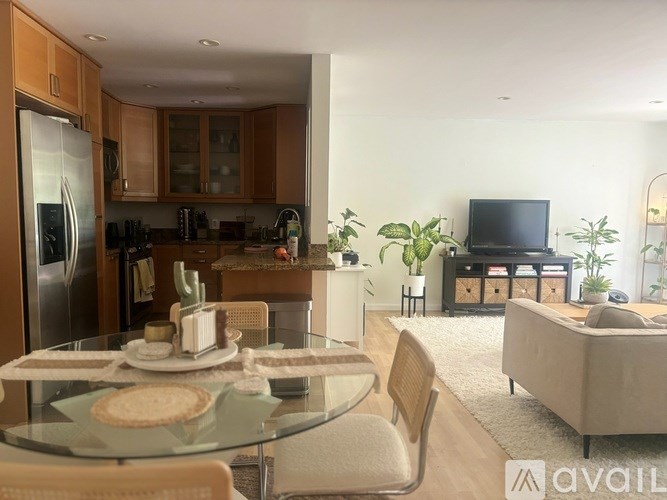 A modern kitchen with a glass table and chairs, a refrigerator, and a television.
