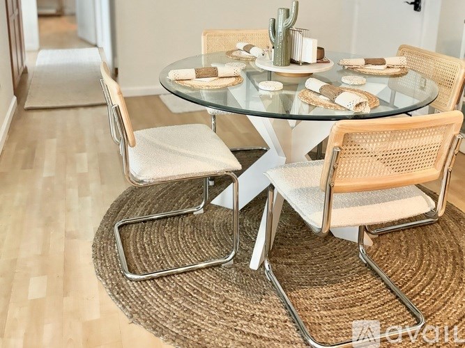 A glass dining table with four chairs and a woven rug in the foreground.