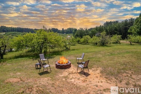A fire pit sits in the middle of a grassy field with two chairs on either side.