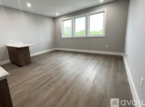 A spacious room with wooden flooring and a window with a view of trees.