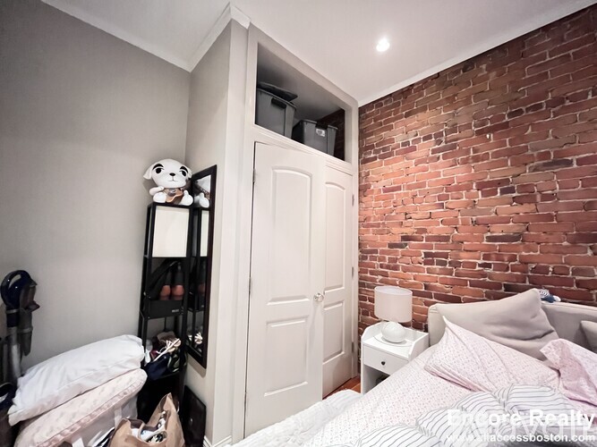 A bedroom with a brick wall and a white bed.