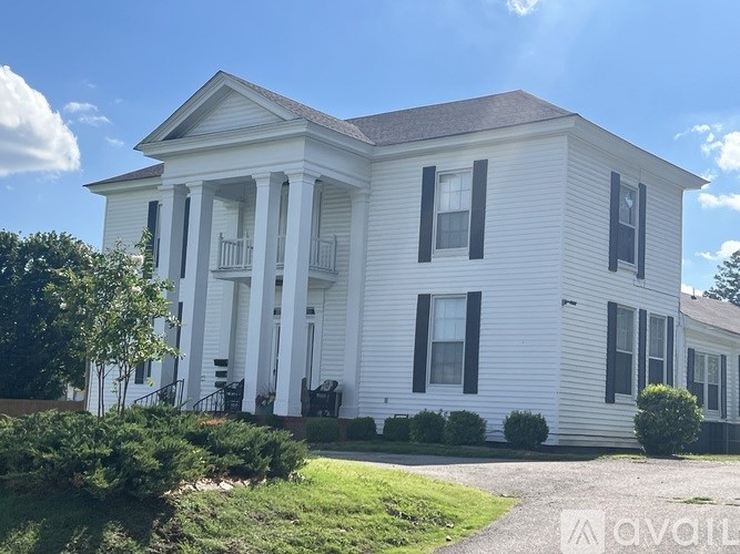 A white house with black shutters and a red brick border.