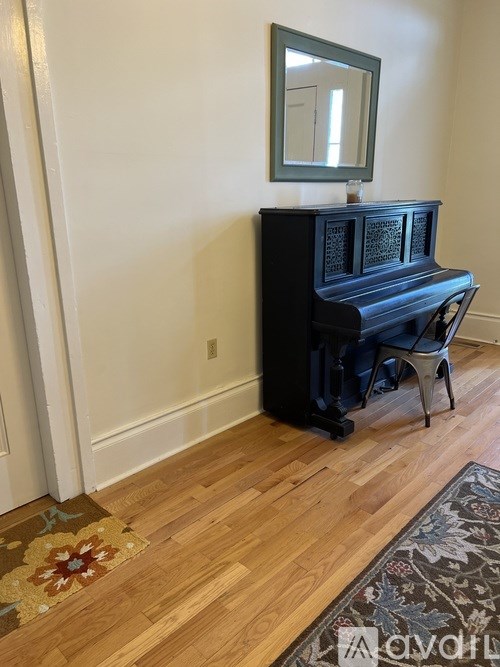 A black piano with a mirror on top is placed in a room with a wooden floor.