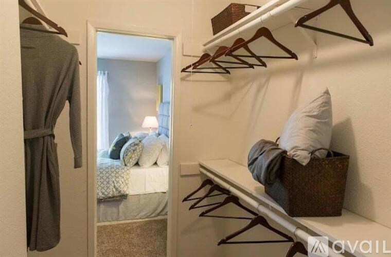 A bedroom with a bed, a bench, and a closet with clothes hanging.