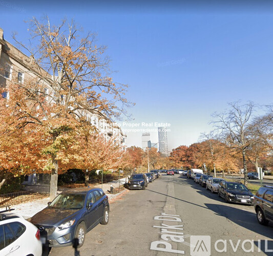 A street view with cars parked on the side and trees with autumn leaves.