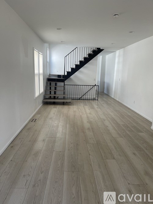 A spacious room with a wooden floor and a staircase with a metal railing.