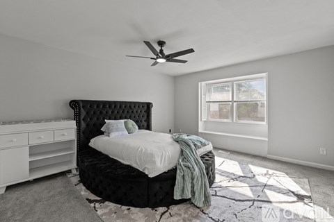 A bedroom with a black headboard bed, a white dresser, and a ceiling fan.