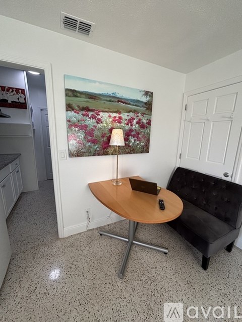 A living room with a black couch and a table with a lamp on it.