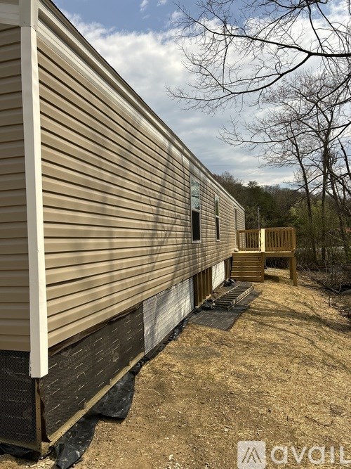 A beige mobile home with a porch and a tree in the background.