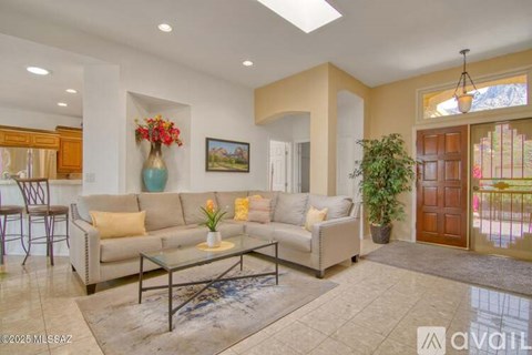 A living room with a beige couch, a glass coffee table, and a painting on the wall.