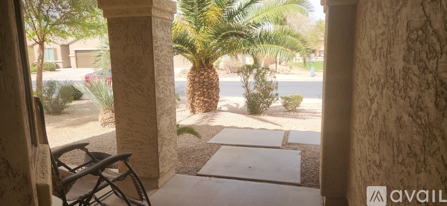 A patio with a chair and a view of a street with cars and palm trees.
