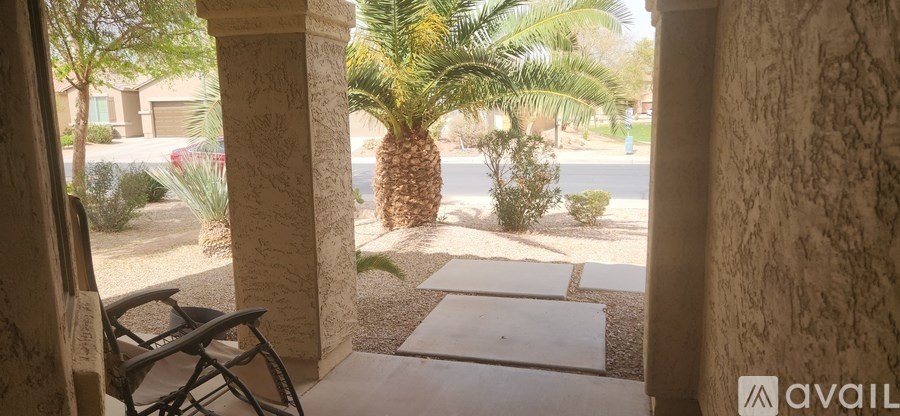 A patio with a chair and a view of a street with cars and palm trees.