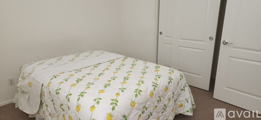 A bed with a white cover and yellow flowers is in a room with two doors.