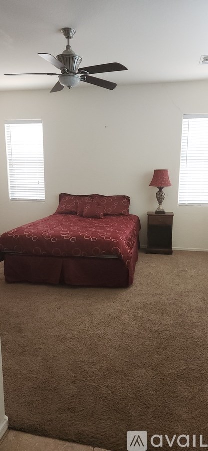 A bedroom with a red bedspread and a ceiling fan.