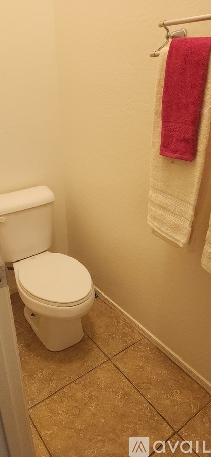 A white toilet in a bathroom with a towel hanging on the wall.
