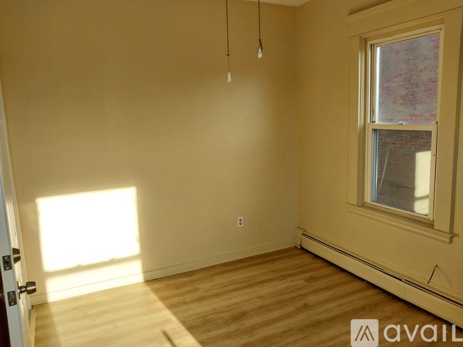 A room with wooden flooring and a window letting in sunlight.