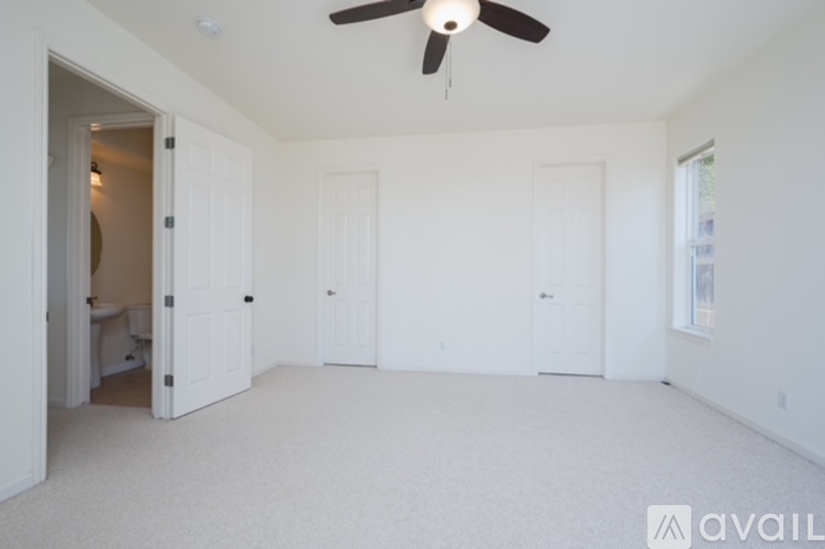 A spacious room with a ceiling fan and three doors.