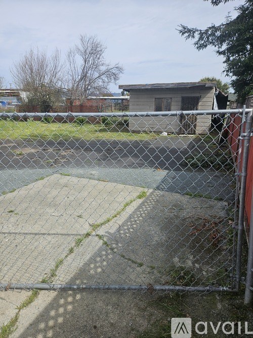 A chain link fence surrounds a concrete area with a building in the background.