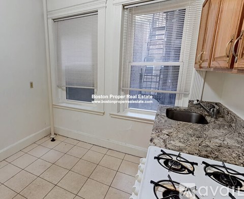 A kitchen with a white stove top and a window with blinds.