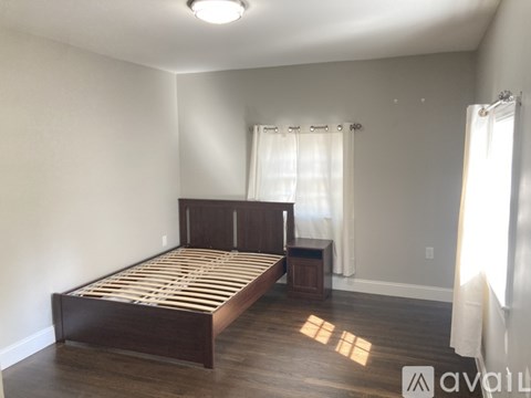 A bedroom with a bed, nightstand, and window with white curtains.