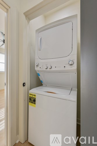 A white dryer is in a narrow space between a door and a wall.