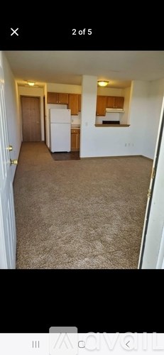 A room with a carpeted floor and a white refrigerator.