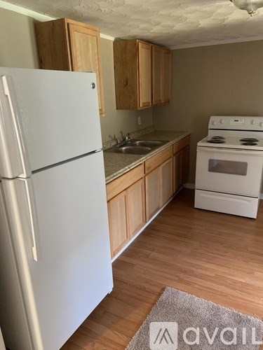 A white refrigerator stands in a kitchen with wooden cabinets and a white stove.