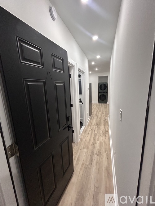 A hallway with a black door and wooden flooring.
