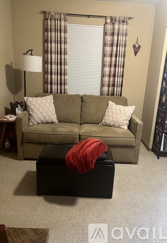 A living room with a couch, ottoman, and lamp.