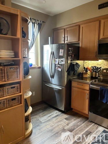 A kitchen with a refrigerator, wooden cabinets, and a stone backsplash.