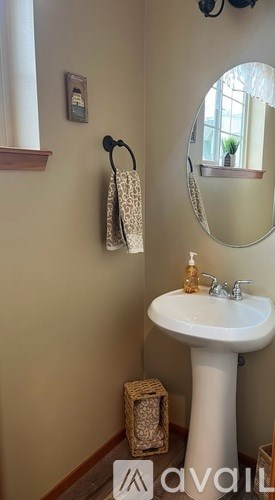A bathroom with a white pedestal sink and a round mirror.