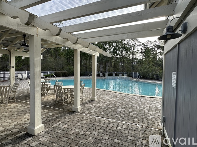A pool area with a white pergola and brick flooring.