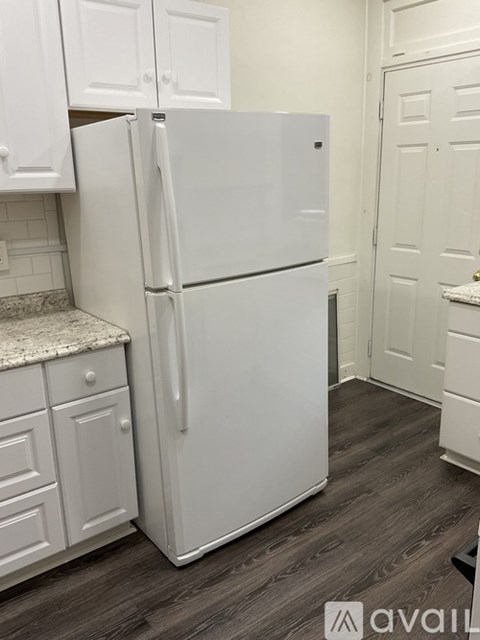A white refrigerator in a kitchen with white cabinets.