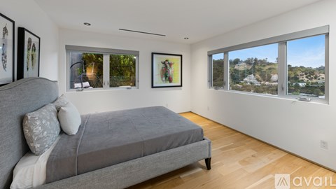 A bedroom with a grey bed and a window overlooking a hilly landscape.