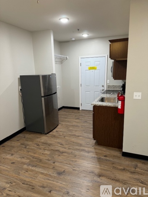 A kitchen area with a black fridge and wooden flooring.