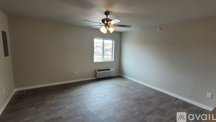 A spacious room with a ceiling fan and a window with an air conditioning unit beneath it.