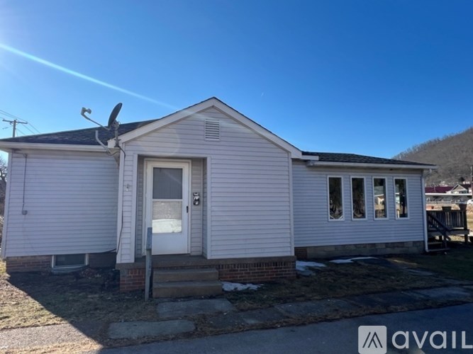 A small white house with a porch and a fan on the roof.