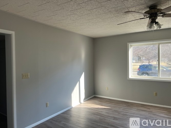 A room with a ceiling fan and a window showing a blue car outside.