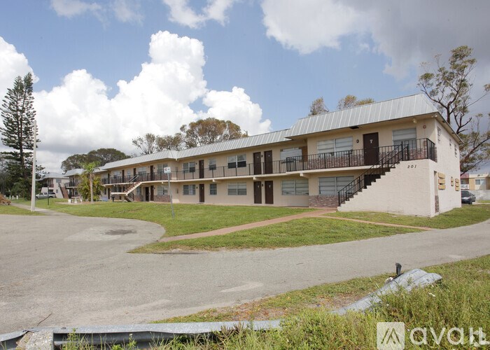 A building with a metal roof and a balcony is surrounded by a grassy area and trees.