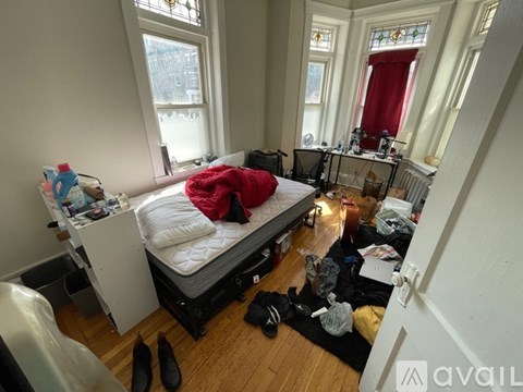 A messy bedroom with a bed in the center and a desk to the left.