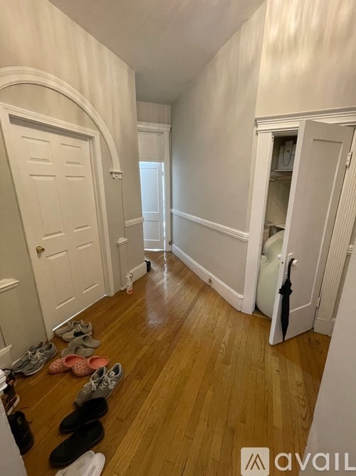 A hallway with white walls and a row of shoes on the floor.