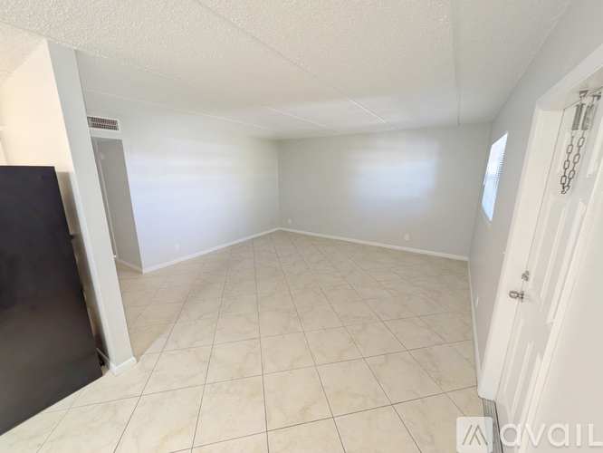 A room with white walls and tiled flooring, with a door on the right and a window on the left.