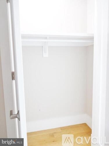 A white door with a silver handle is open to a room with white walls and a wooden floor.