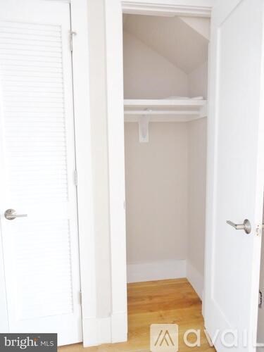 A white door is open to a small, empty room with a wooden floor.