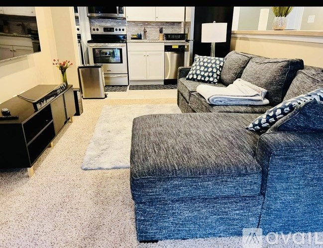 A grey couch with a white pillow and a grey blanket on it.