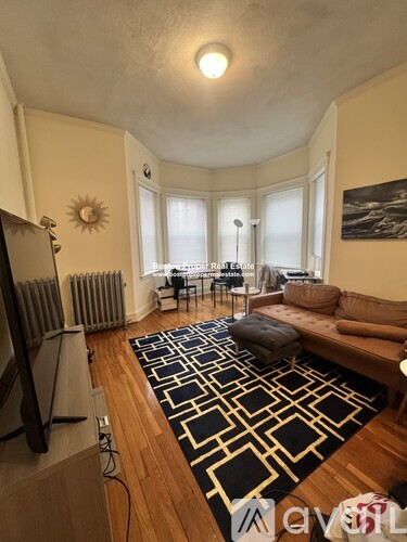 A living room with a black and white rug, a brown couch, and a flat screen TV.
