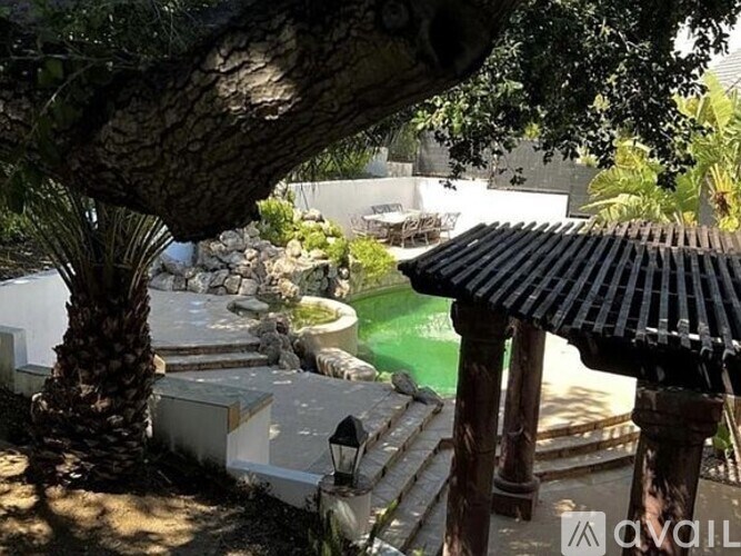 A gazebo sits in the middle of a garden with a pool.