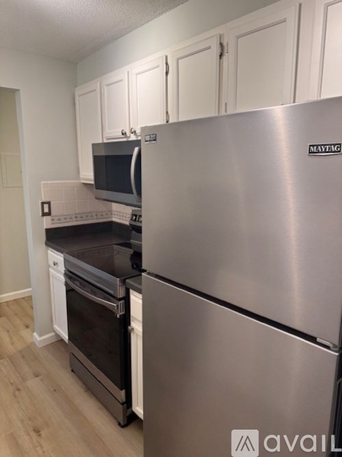 A Maytag refrigerator stands in a kitchen with white cabinets and black countertops.